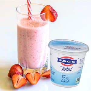 greek yogurt smoothie in a glass with a tub of Fage yogurt and strawberries around