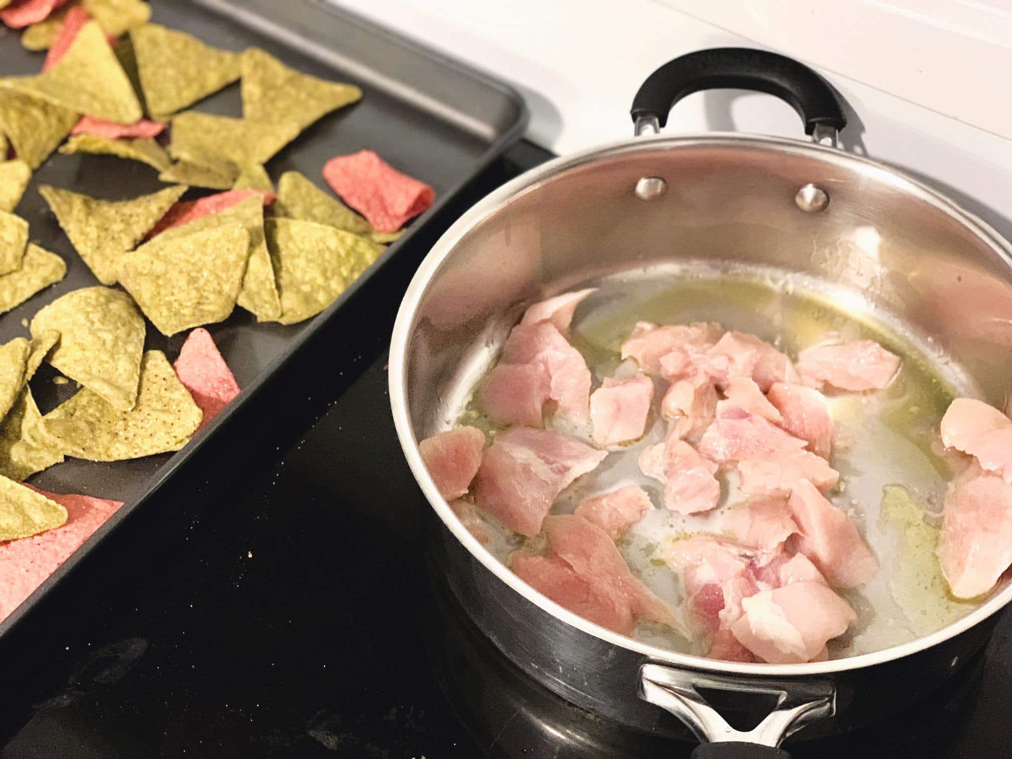raw chicken cooking in a skillet next to tortilla chips on a sheet pan
