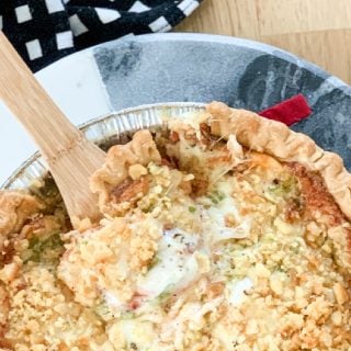 Savory Southern Tomato Pie in a foil pan with a wooden spoon