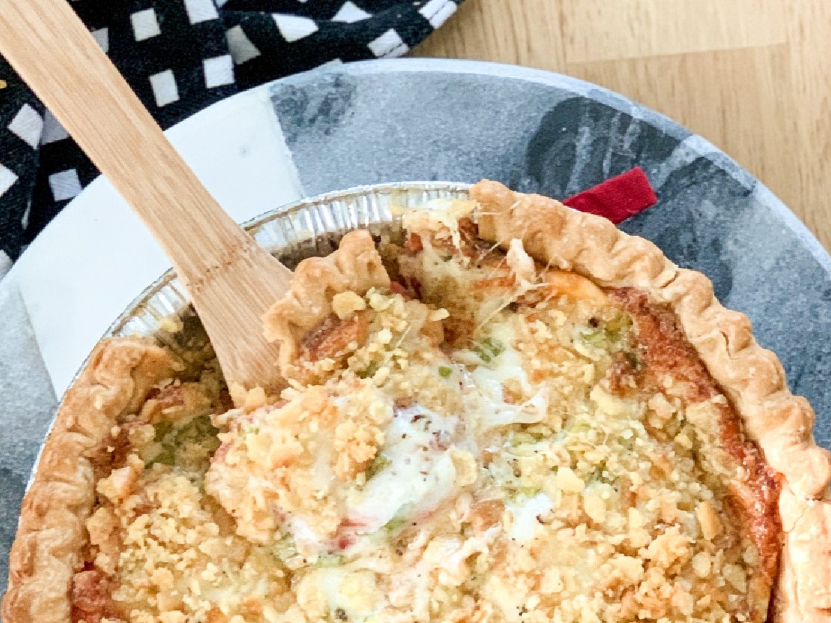 Savory Southern Tomato Pie in a foil pan with a wooden spoon