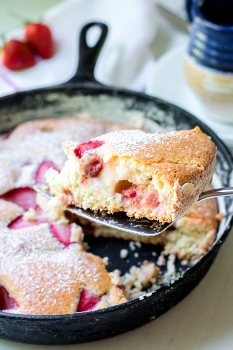 swlice of strawberry cake on pie server with full cake in a cast iron pan in the background