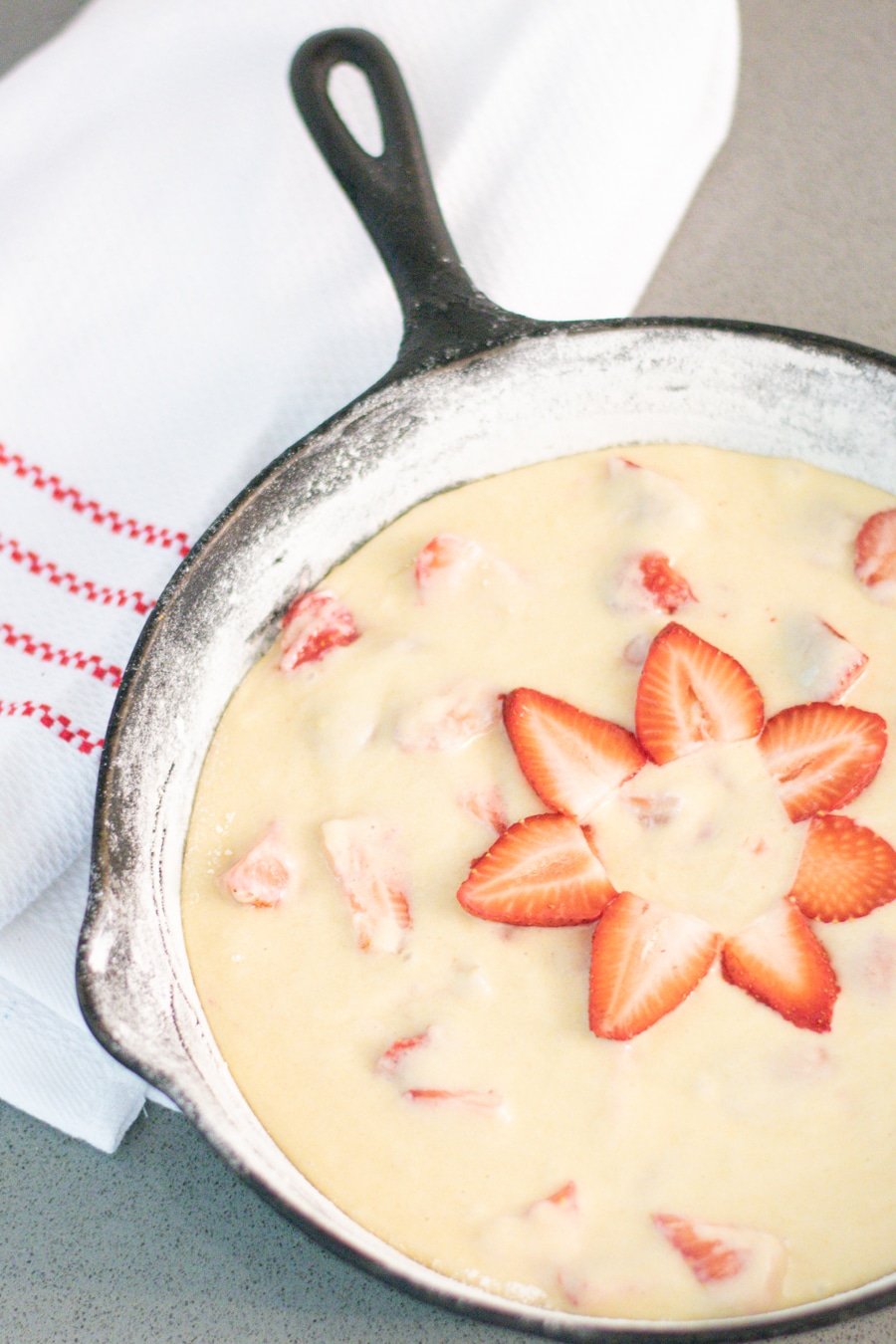 strawberry cake batter in a cast iron pan with strawberry slices in the shape of a flower on top