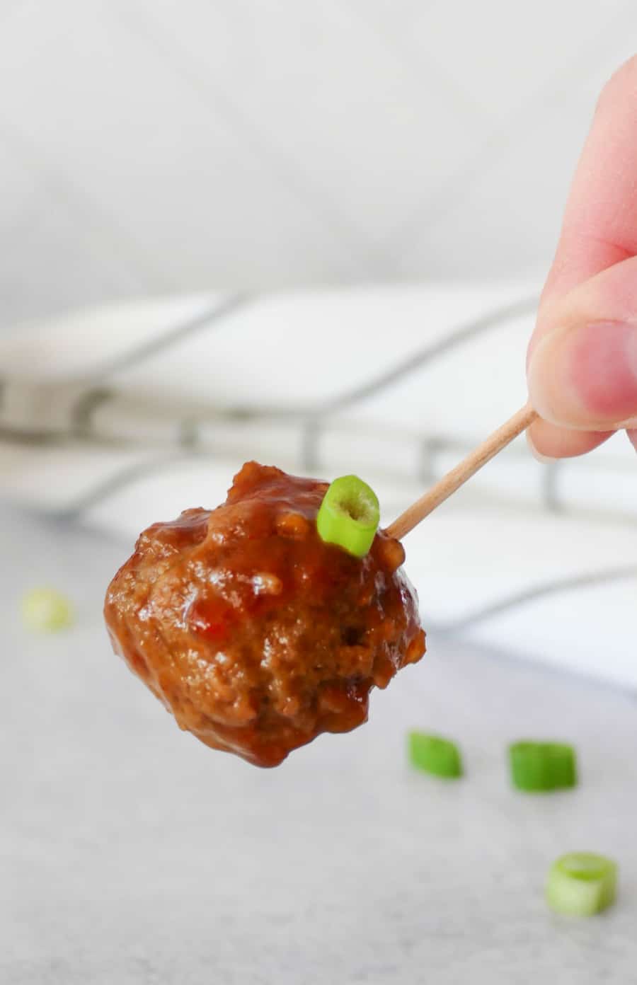 hand holding a meatball on a toothpick with sauce and green onion garnish