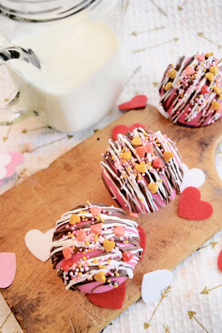 3 hot chocolate bombs for Valentine's Day on a wood board with a mug of milk