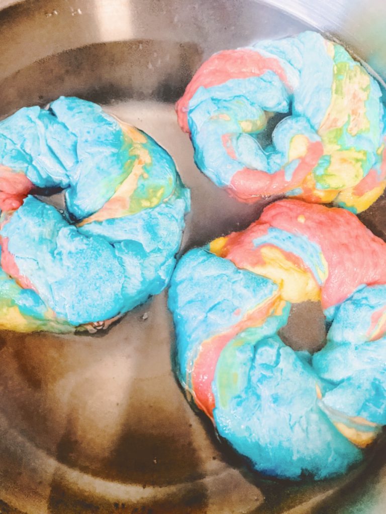 three rainbow bagels boiling in a pot of water