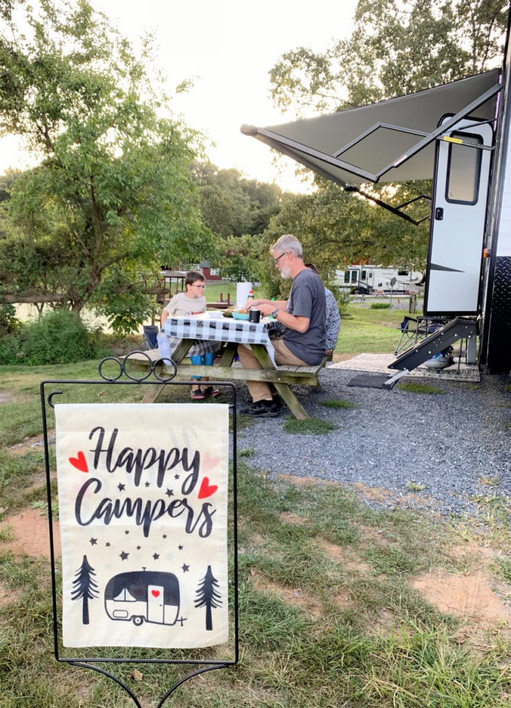 Happy RV Campers flag with family eating near RV in the background