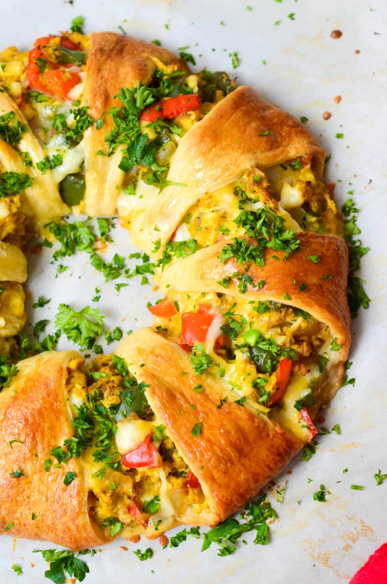 A crescent roll ring with vegetables and herbs on a baking sheet.