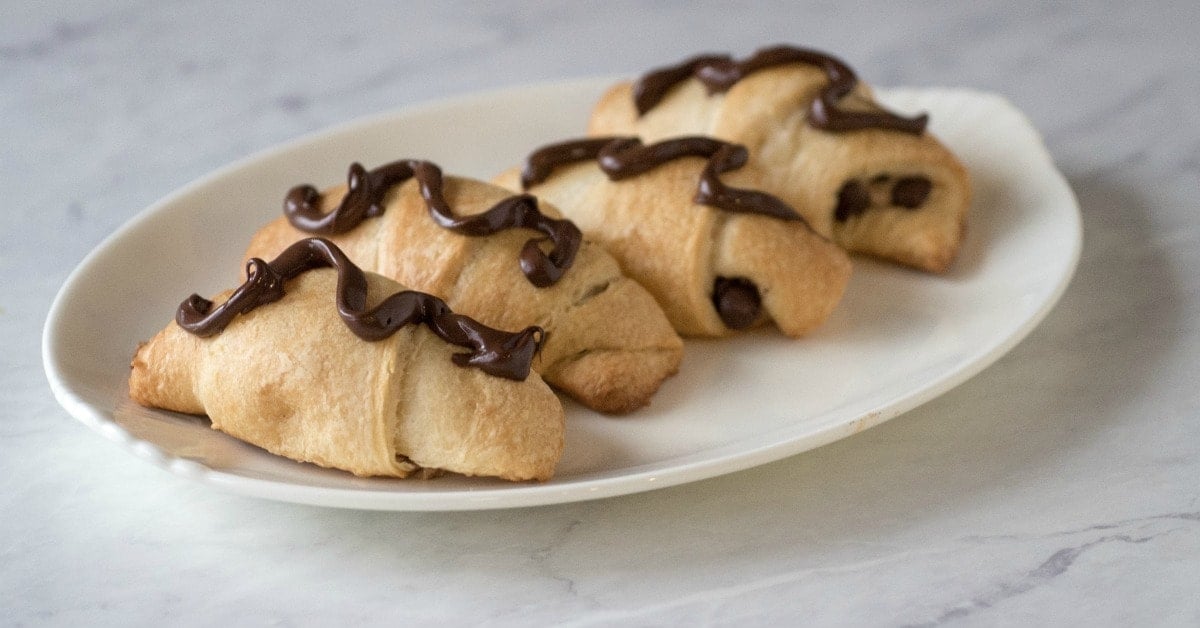 Three chocolate croissants on a white plate.
