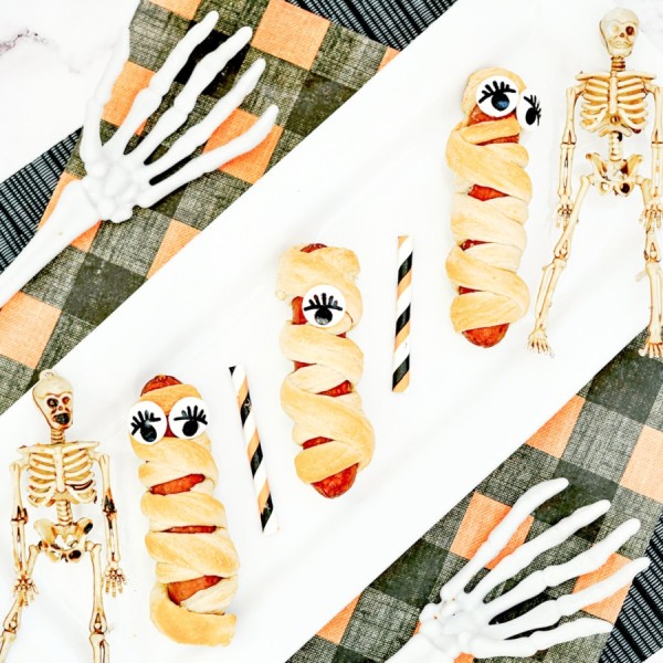 Mummy dogs recipe on a platter with decorative skeletons