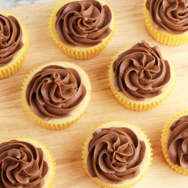 Eight vanilla cupcakes with chocolate frosting, made using an easy chocolate frosting recipe, are expertly arranged on a wooden board.