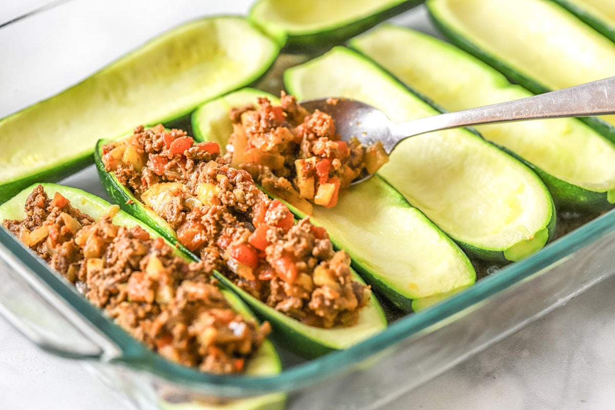 spoon cooked taco filling into zucchini boats