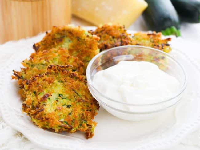 Panko Zucchini Fritters arranged on a plate with a bowl of sour cream