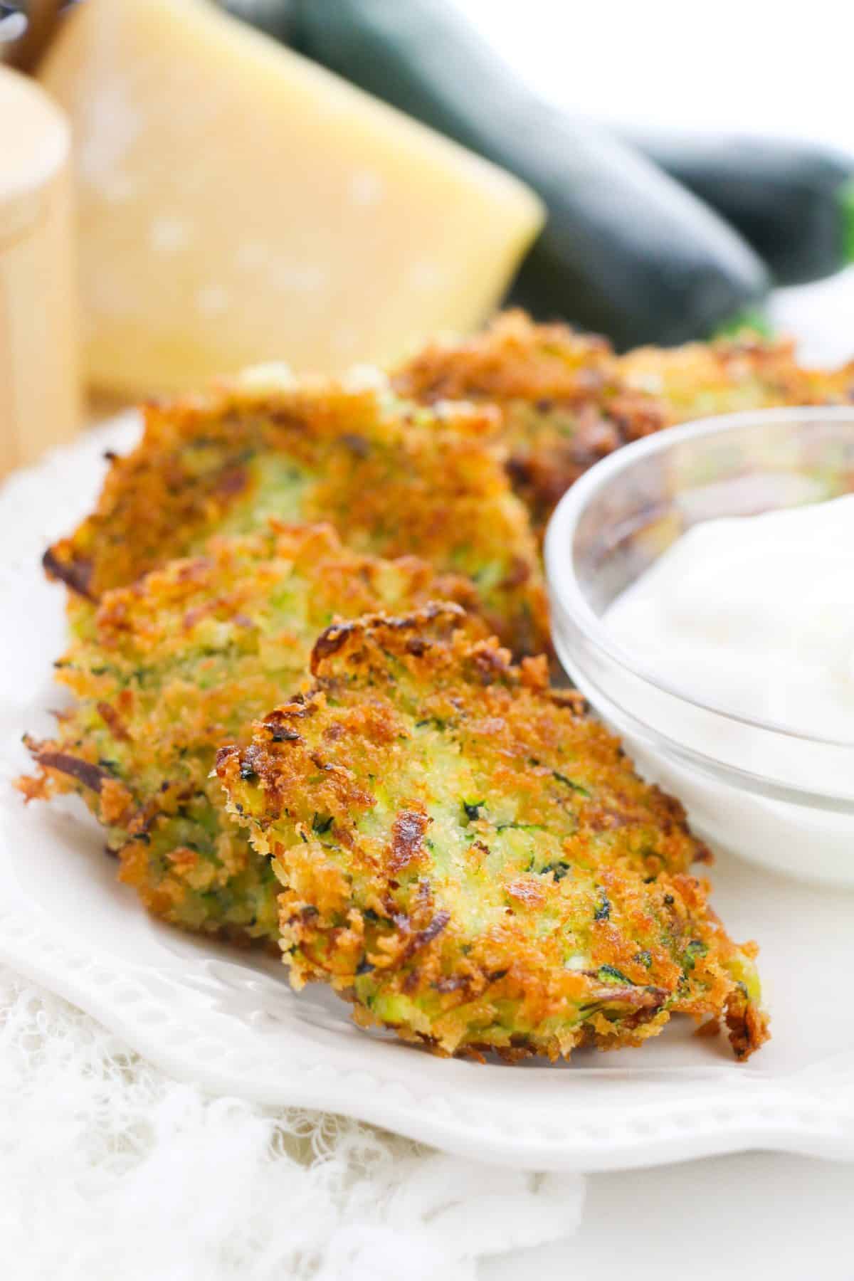 zucchini fritters on a plate with a small bowl of dipping sauce