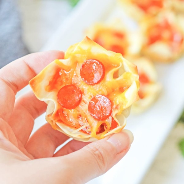 Muffin tin Pizza Wonton Cups in the background with a hand holding one close up