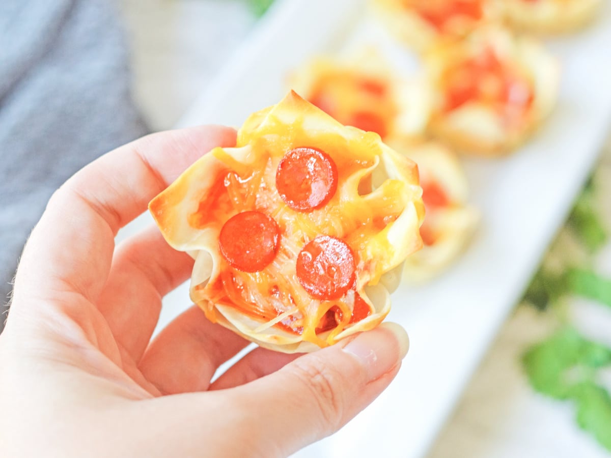 Muffin tin Pizza Wonton Cups in the background with a hand holding one close up