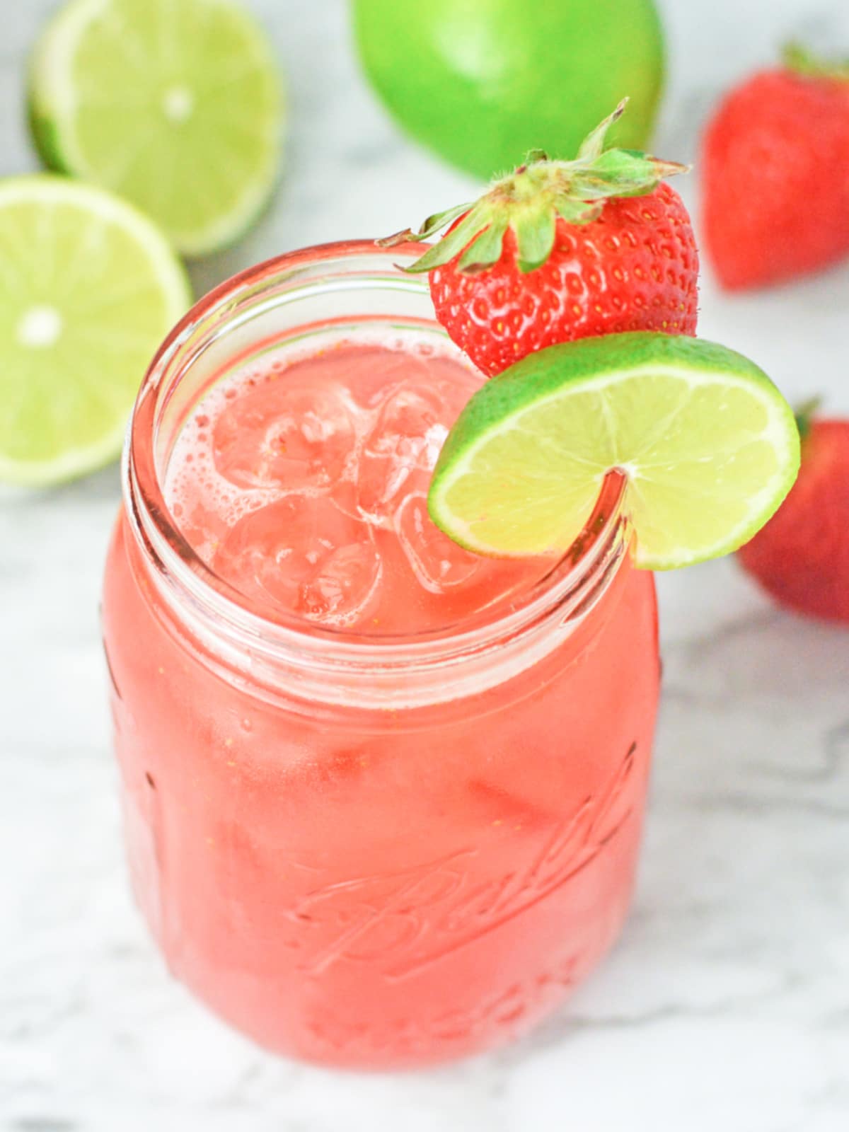 strawberry agua fresca in a glass over ice with strawberry and lime garnish