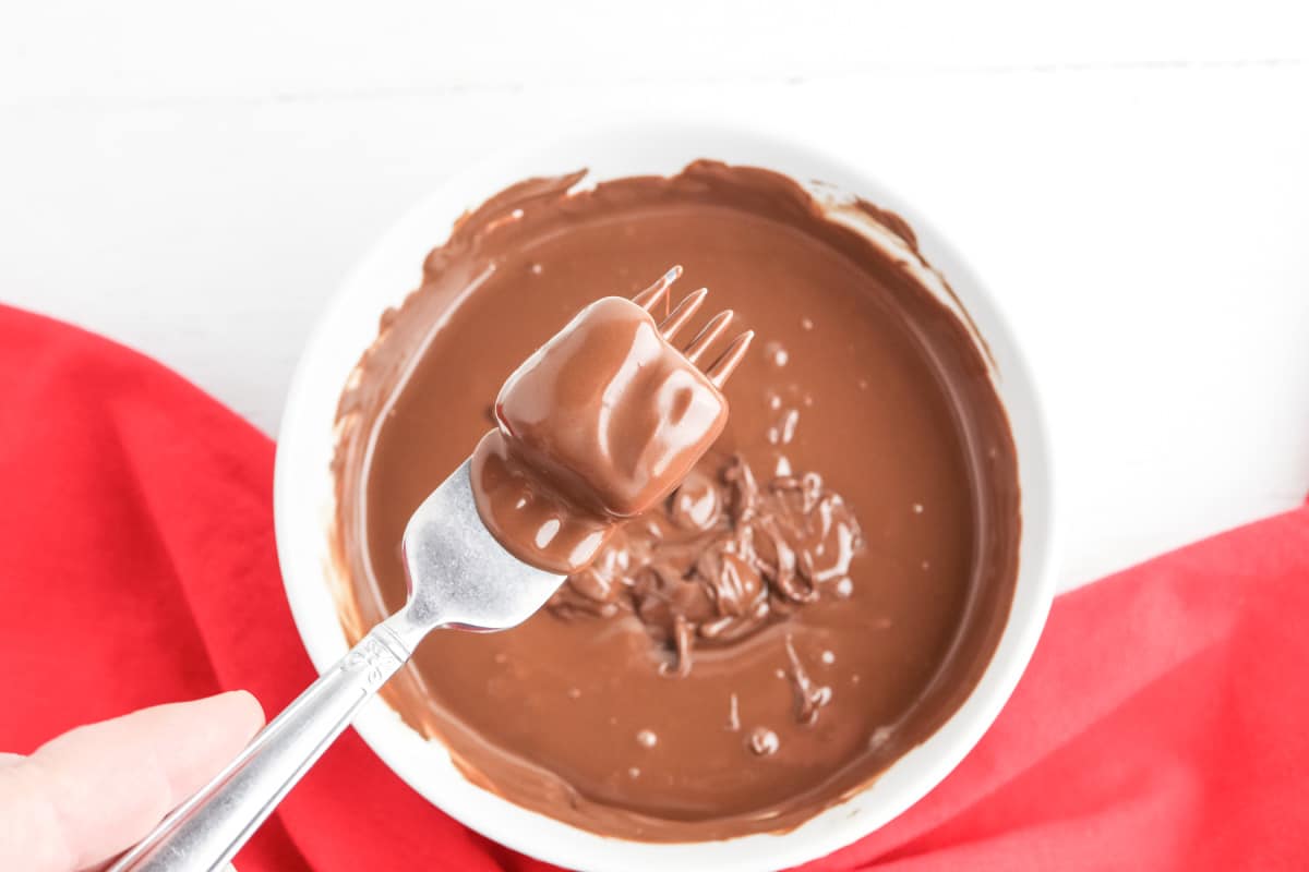 dip candy in bowl of melted chocolate with fork