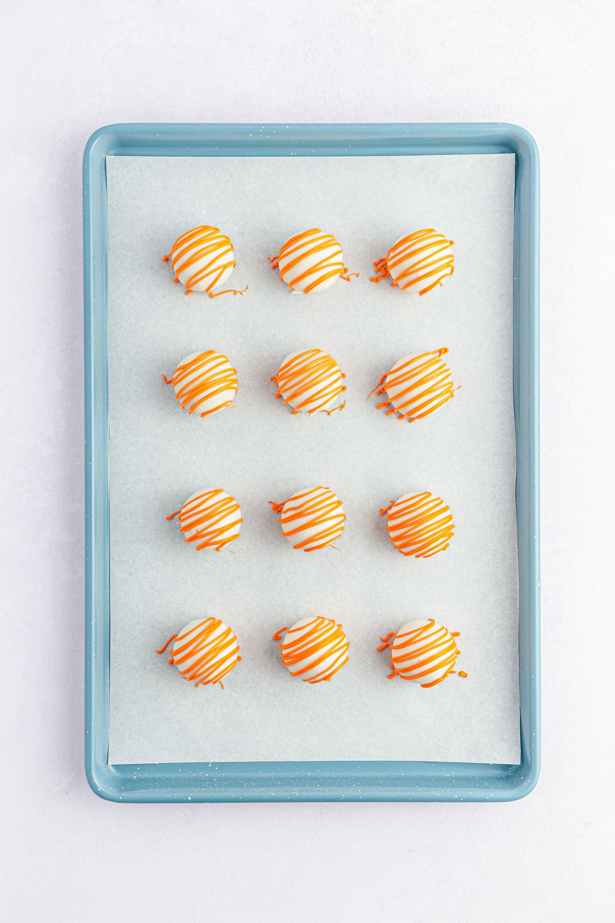orange drizzle on carrot cake balls lined on cookie sheet.