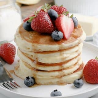 pancakes with syrup blueberries and strawberries on a white plate with a fork
