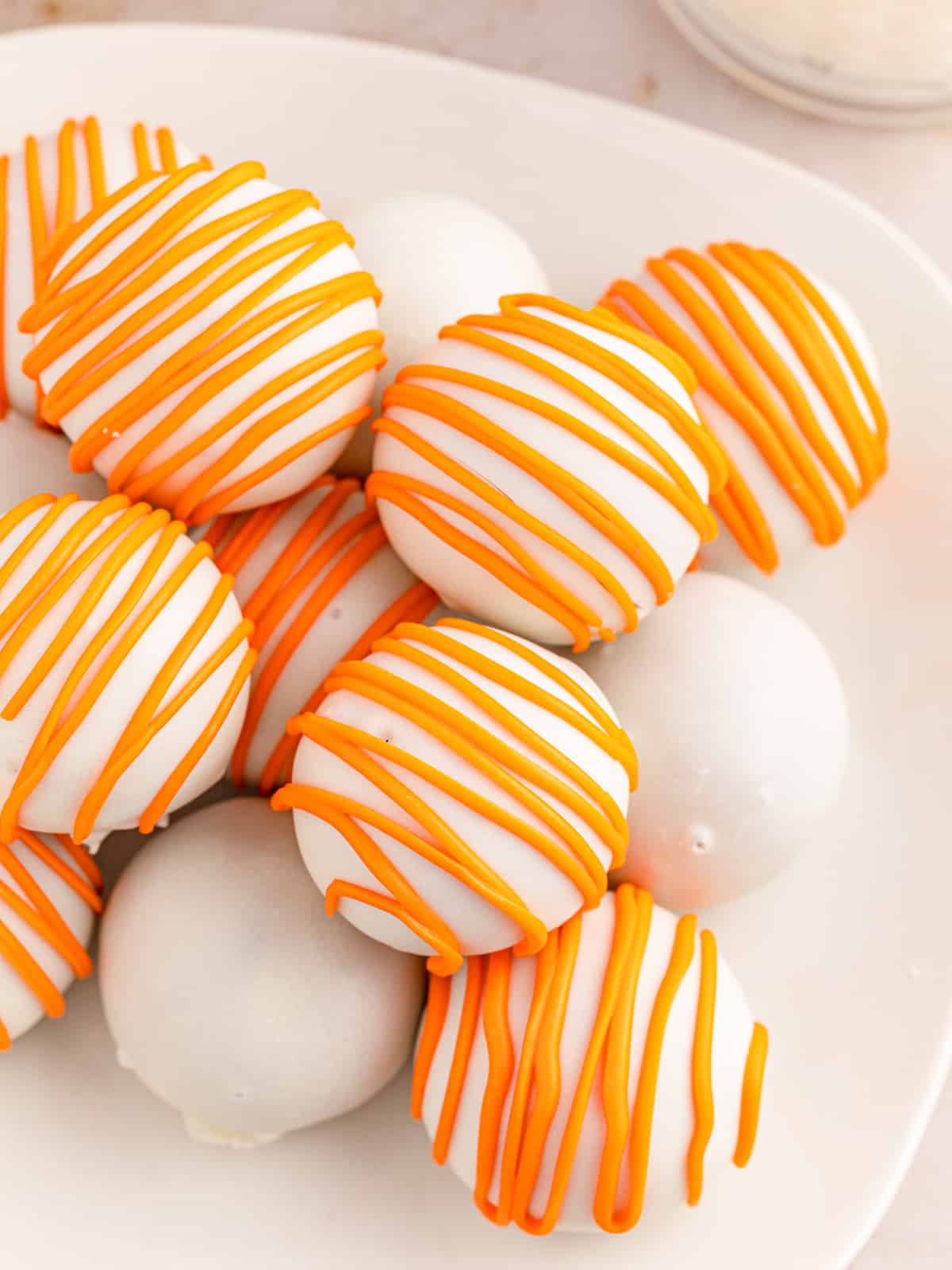 White chocolate dipped carrot cake balls with orange chocolate drizzle on a plate.