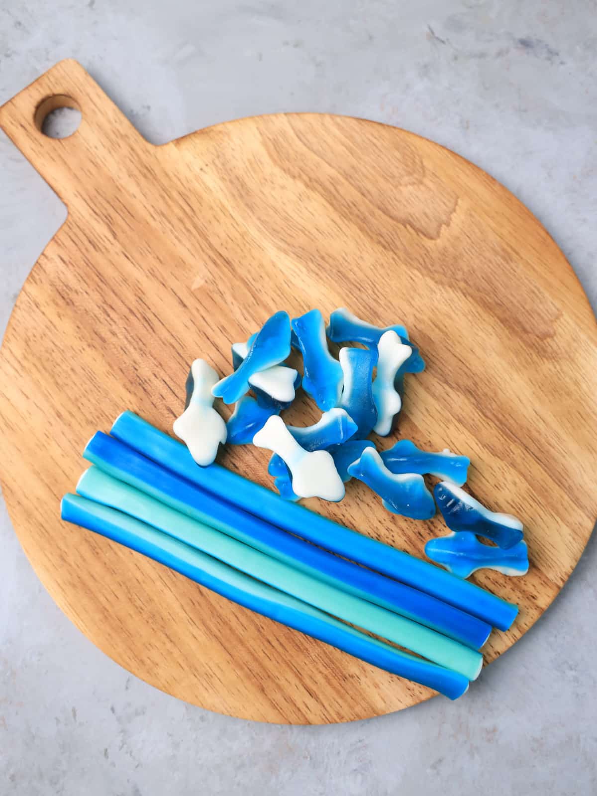 A wooden cutting board with blue and white gummy shark candy on it.