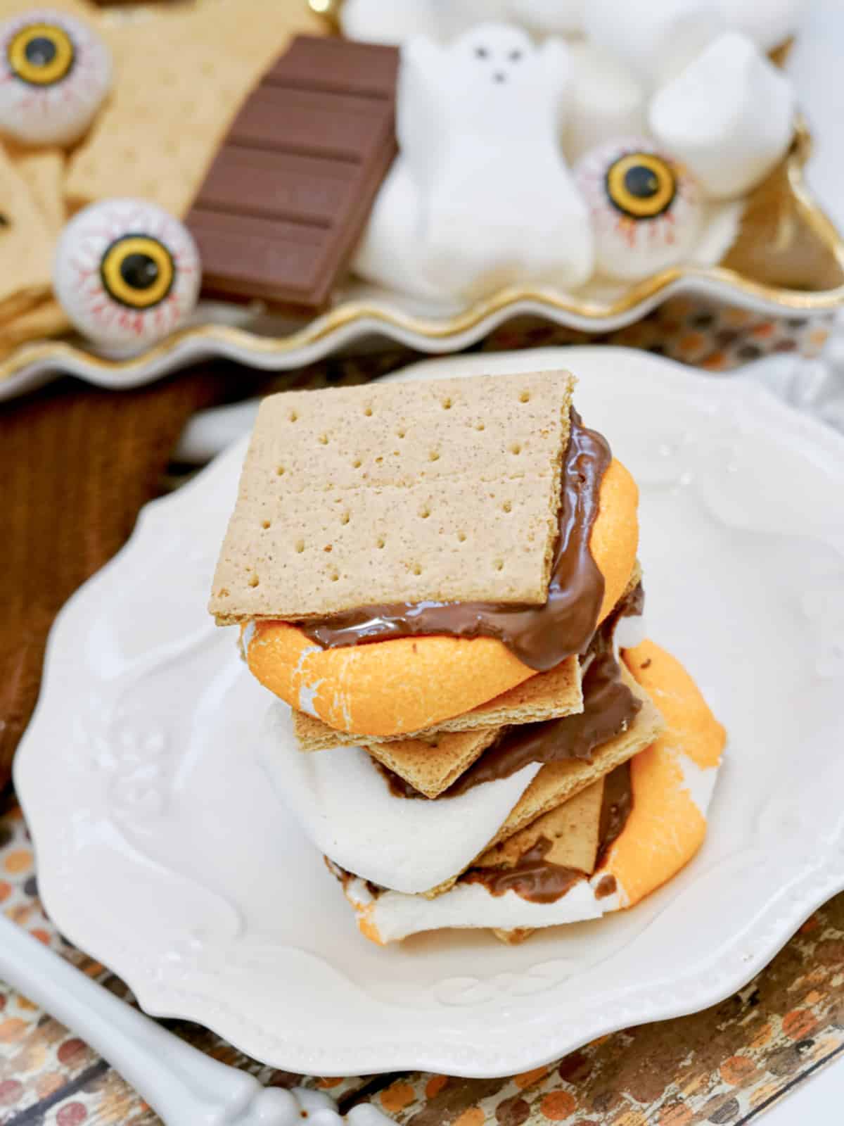 two finished orange and white smores stacked on a white plate surrounded by halloween decorations