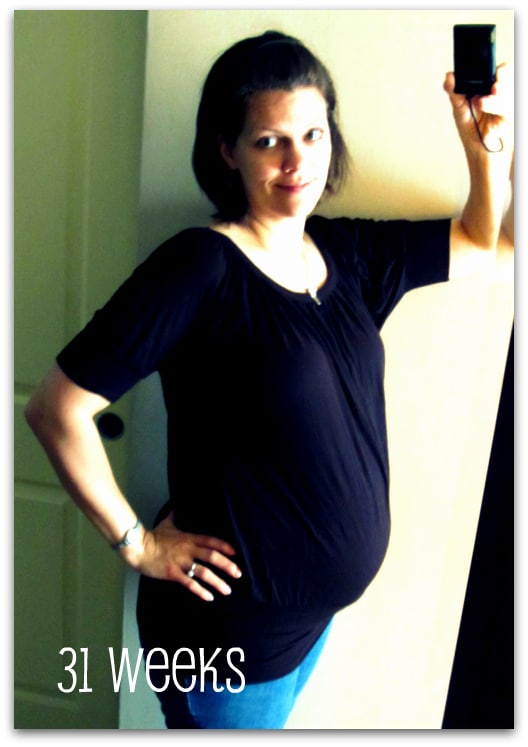 A woman 32 weeks pregnant standing in front of a mirror holding a cell phone.