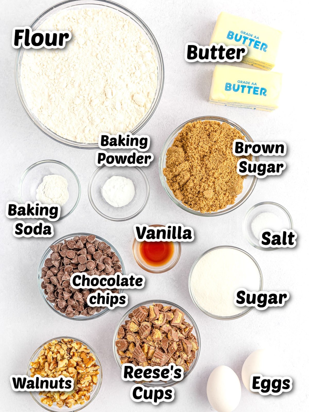 Ingredients for baking laid out on a table, including flour, butter, brown sugar, vanilla, eggs, and other items, each labeled with their respective names.
