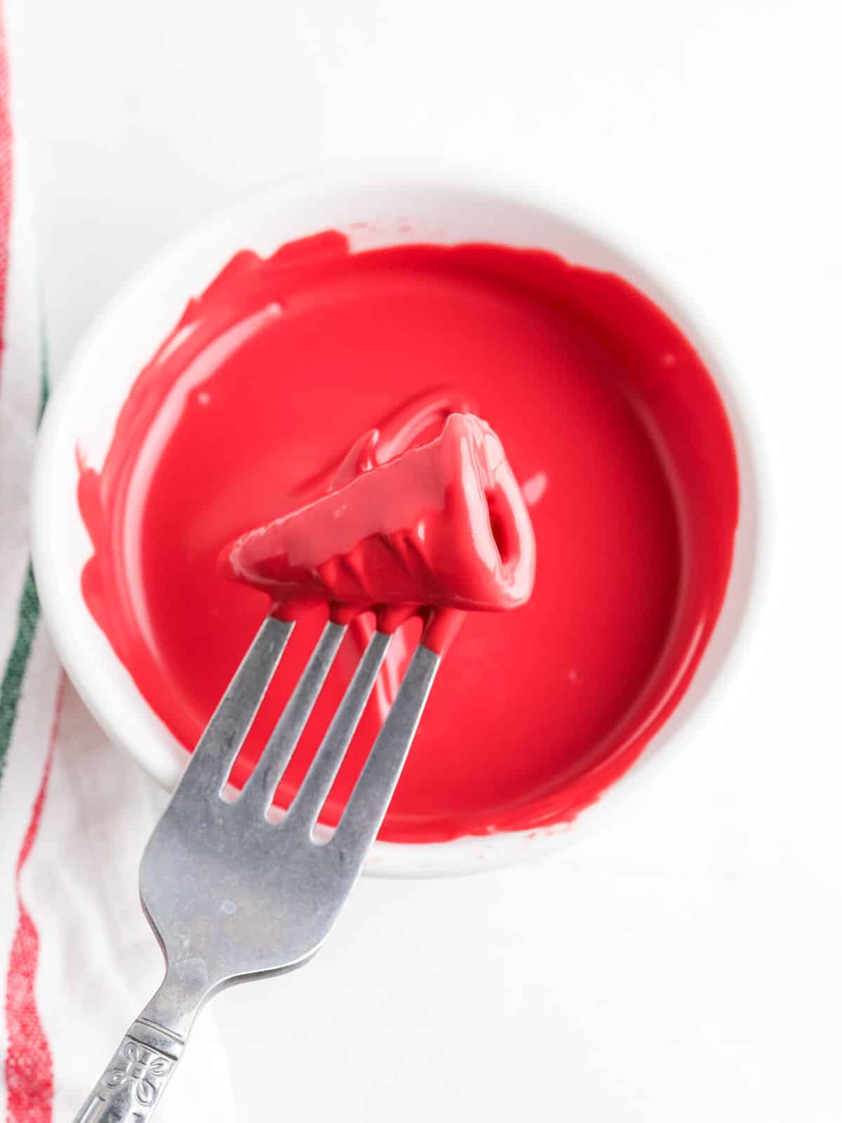 A fork with a Bugle dipped in red melted chocolate over a white bowl.