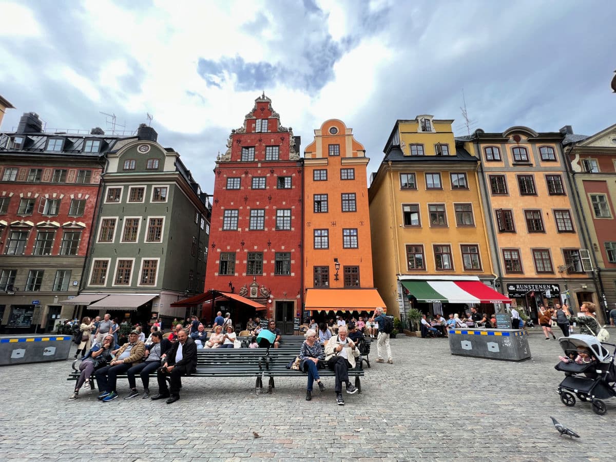 A group of people sitting on a bench in front of colorful buildings.