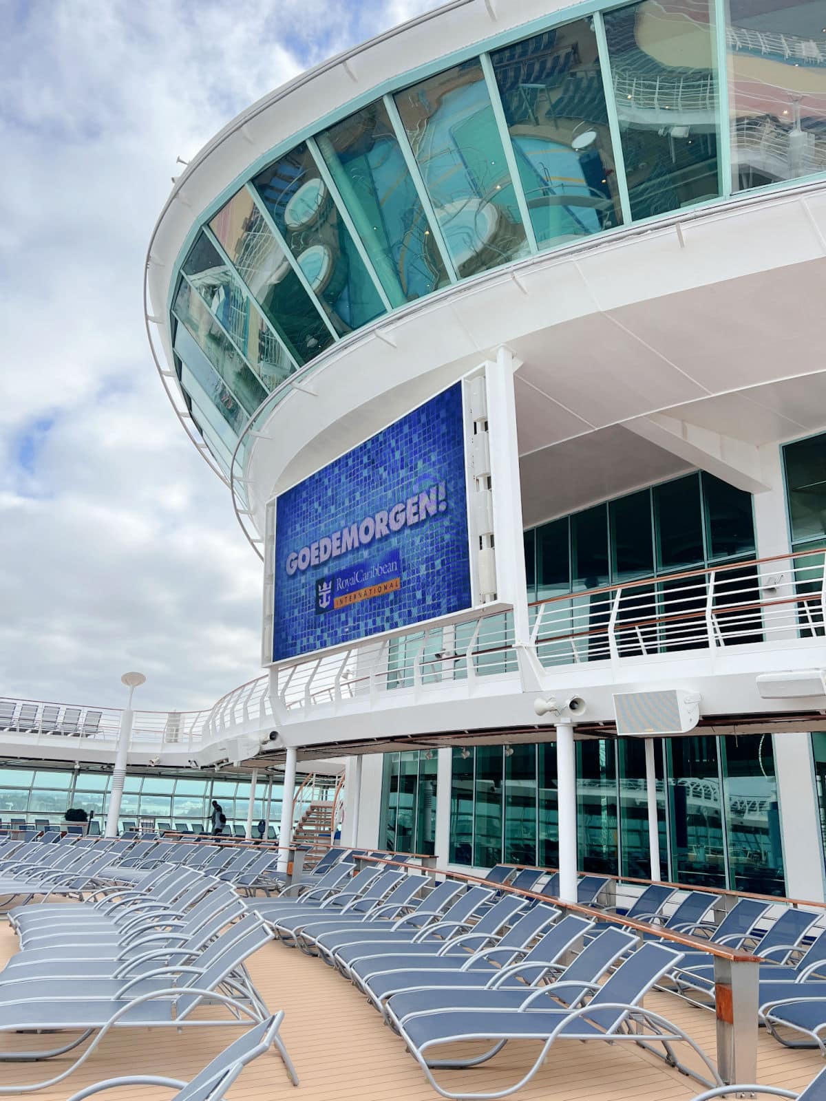 The deck of a cruise ship with lounge chairs and a large screen.