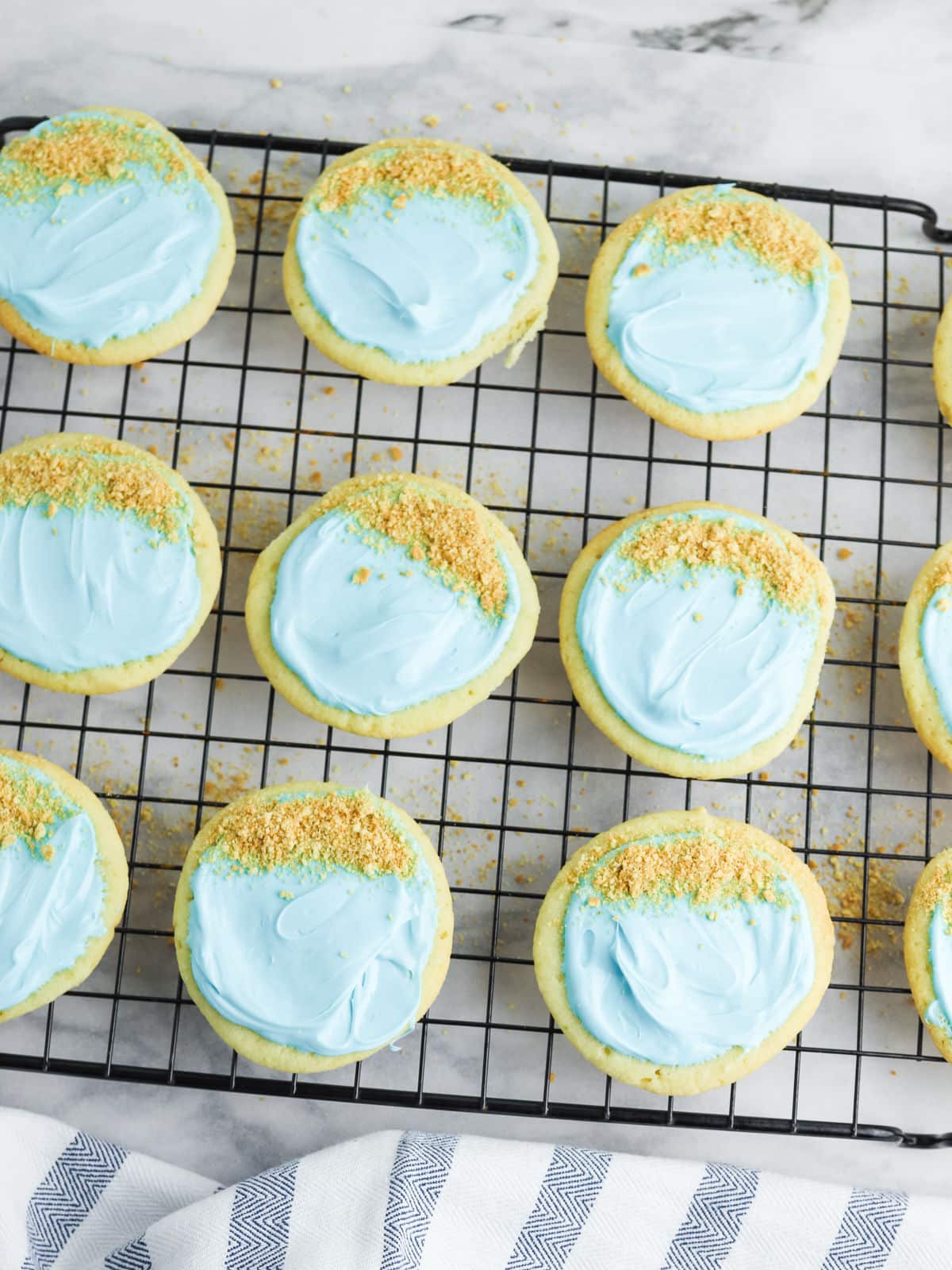 Cookies with blue icing and graham cracker crumbs on a cooling rack.