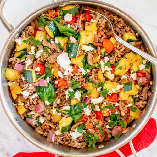 A skillet filled with a colorful ground meat and vegetable stir-fry, garnished with herbs and cheese.
