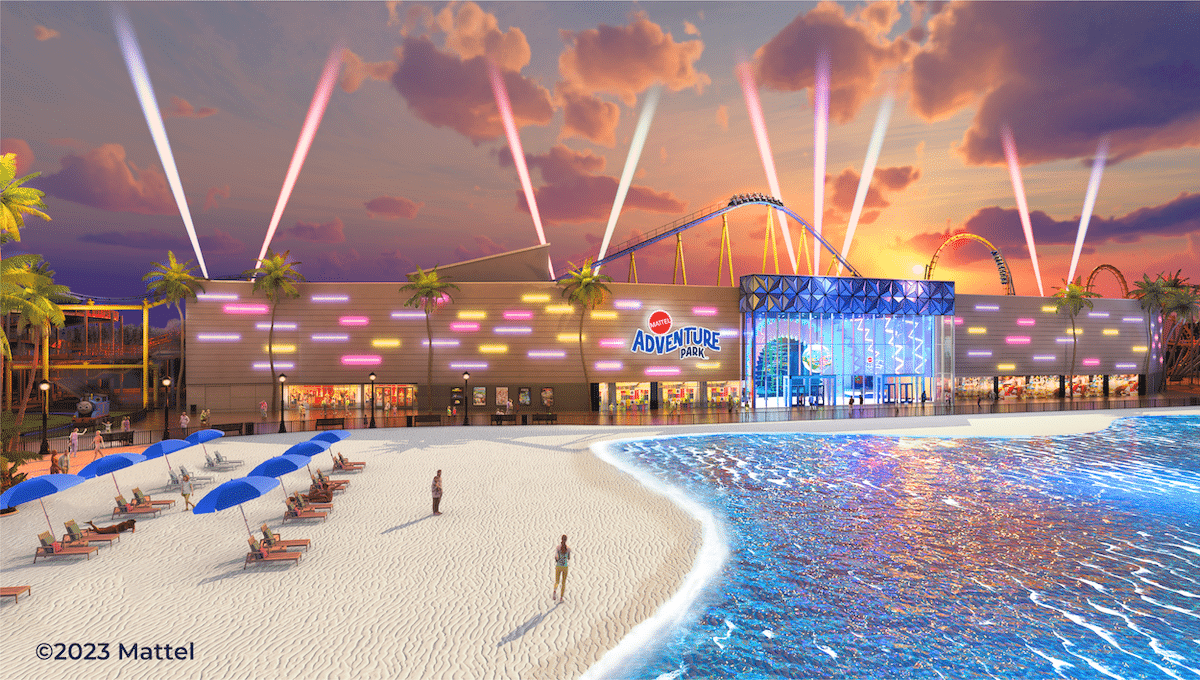 An illuminated entertainment complex by the beach with a roller coaster and spotlights at dusk.