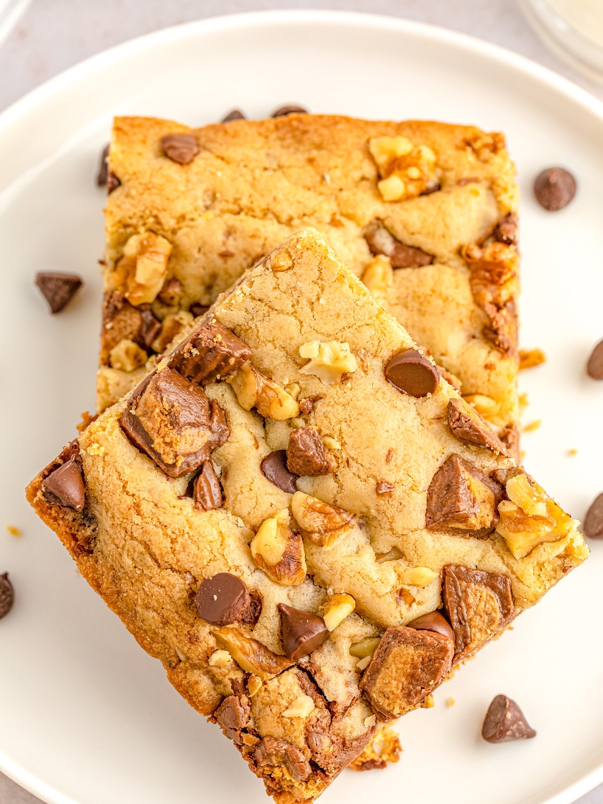 Two peanut butter cup and chocolate chip blondies with walnuts, stacked on a white plate.