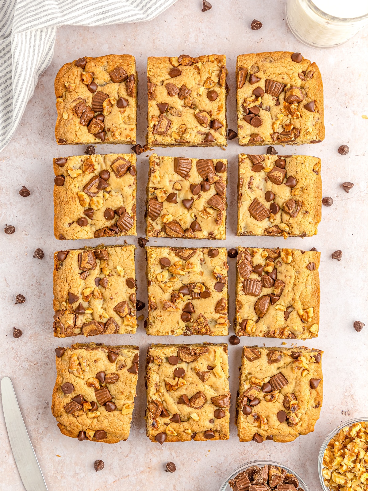 Nine golden-brown blondie bars topped with nuts and chocolate chunks, arranged in a grid on a light surface.