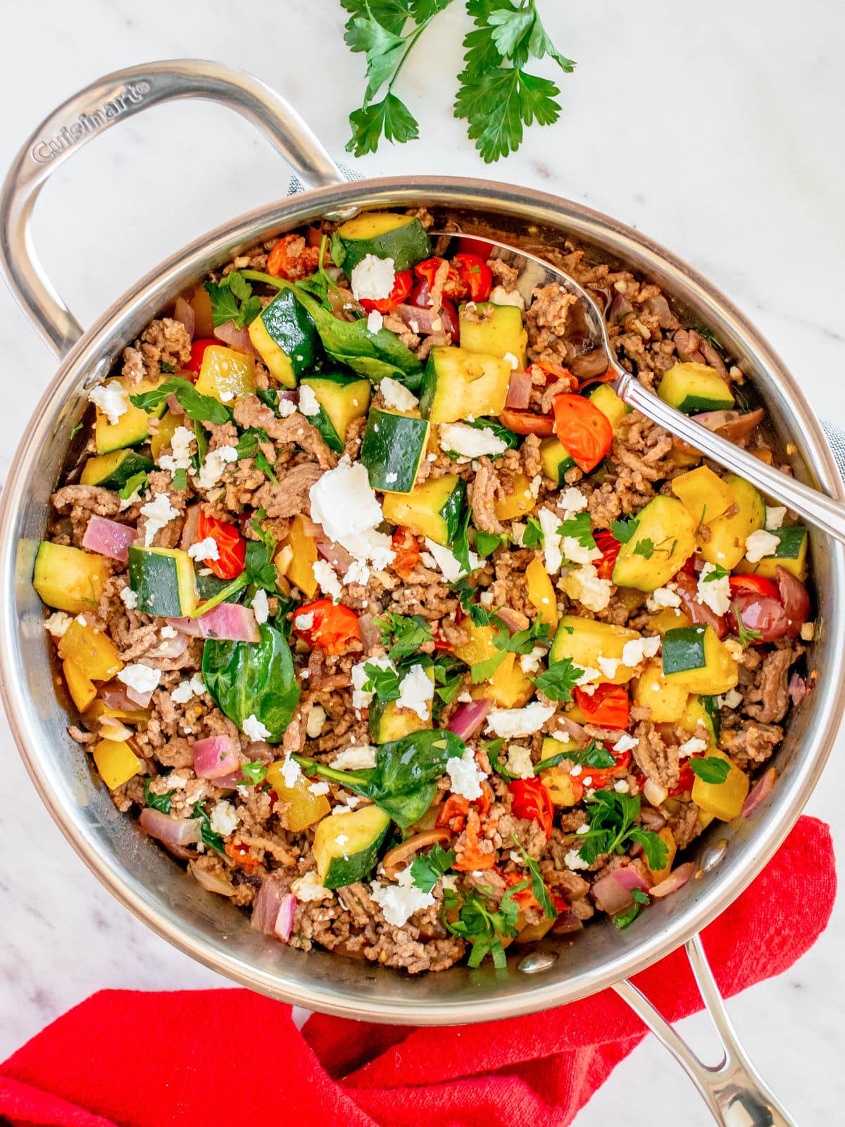 A colorful skillet meal with ground meat, diced vegetables, herbs, and crumbled cheese.