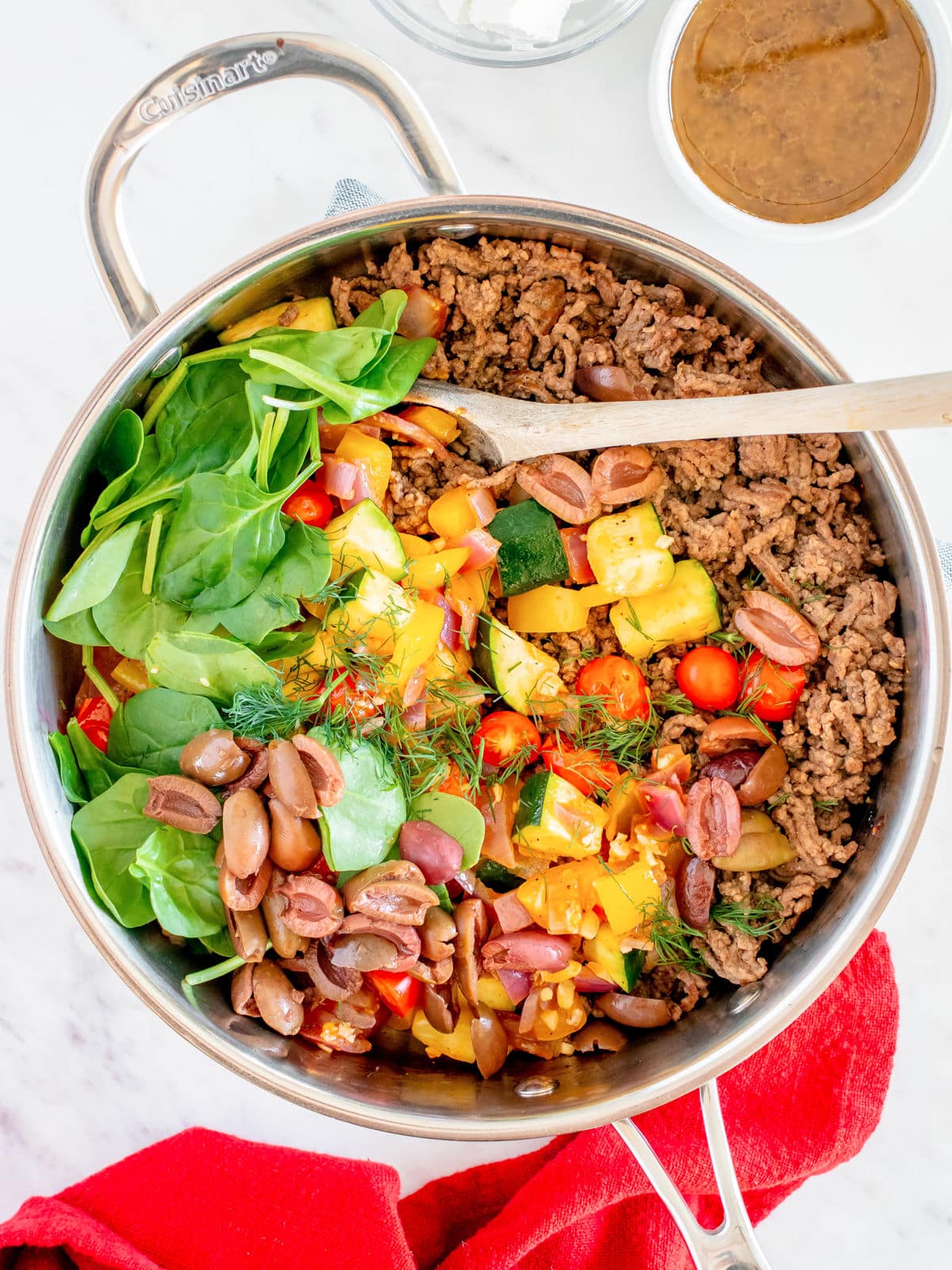 A colorful one-pot meal with ground meat, fresh spinach, cherry tomatoes, diced yellow bell peppers, and kidney beans, garnished with dill, ready to be served.