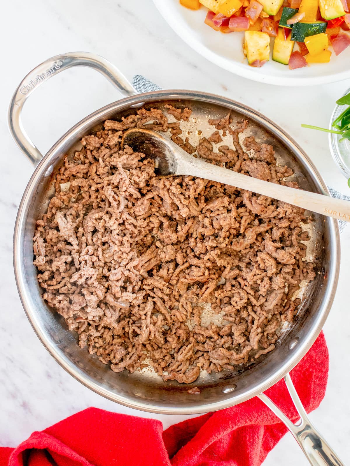 Cooked ground beef in a stainless steel pan with a wooden spoon.