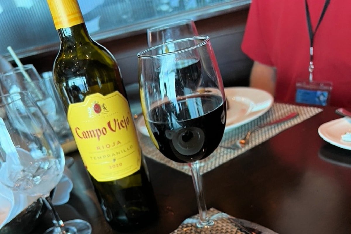A bottle of campo viejo rioja wine beside a filled glass on a restaurant table, with a blurred person in the background.