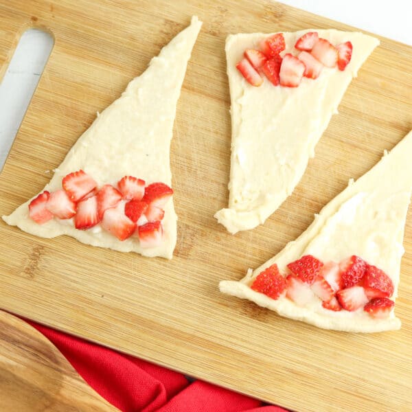 Slices of cheesecake with strawberry toppings on a wooden cutting board.