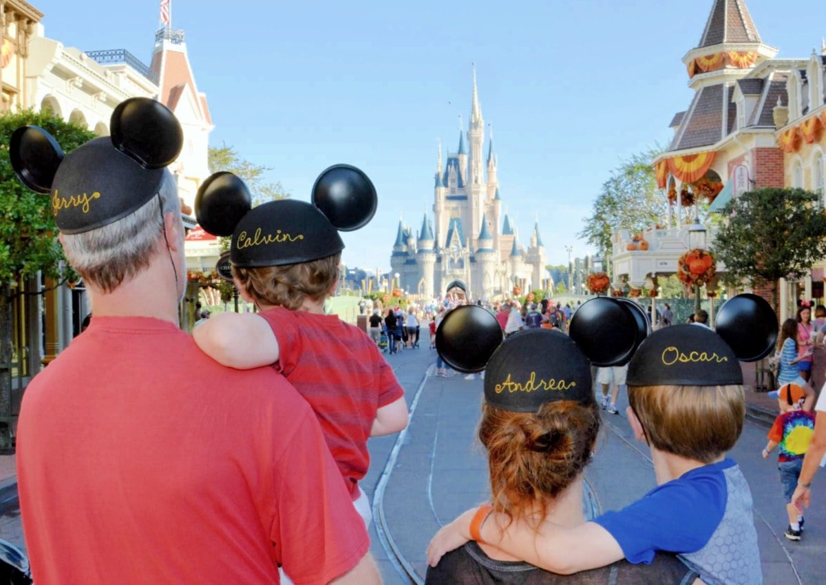 Family of five wearing personalized mickey mouse ears while walking towards cinderella castle at disney world.
