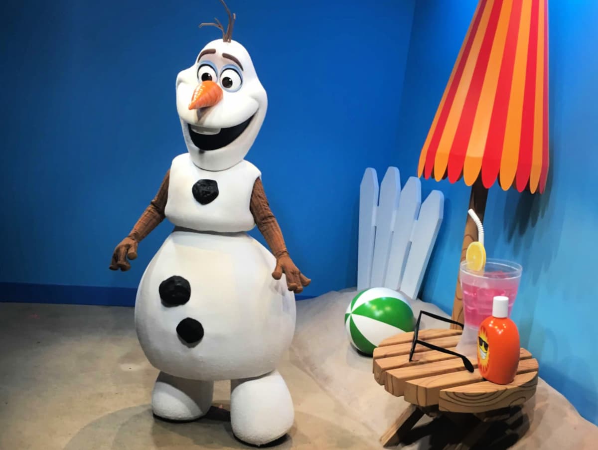 Life-size olaf figure from disney's frozen beside a beach setup with umbrella, chair, beach ball, and drink.