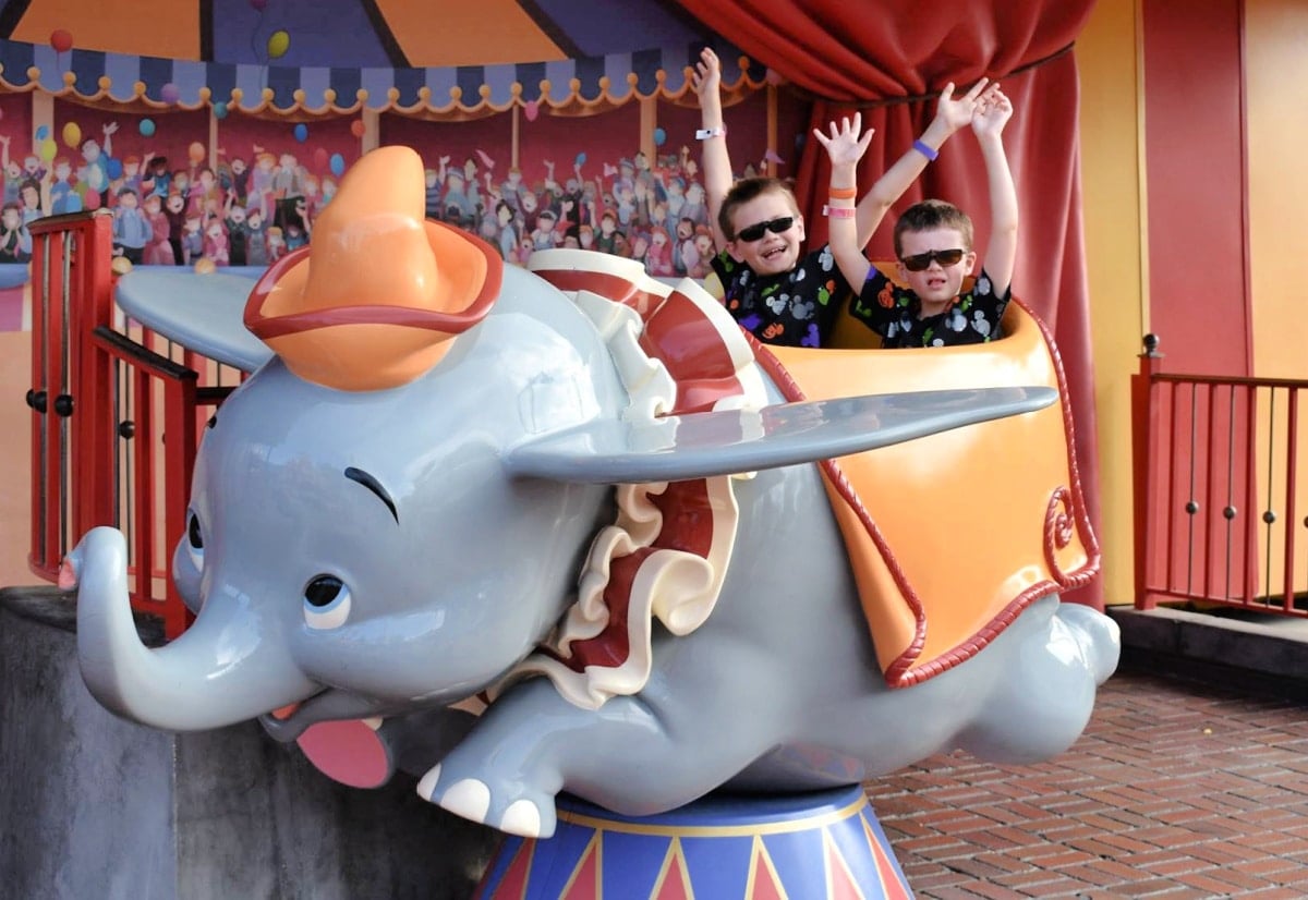 Two people joyfully raising their hands while riding on a dumbo the flying elephant amusement park ride.