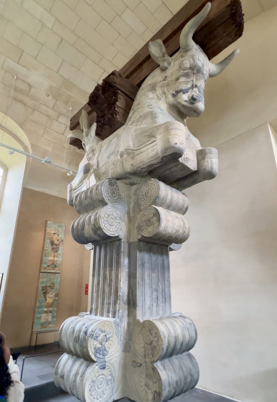 A large stone column capital featuring two bull figures back to back, displayed in a museum setting with a high vaulted ceiling—an architectural marvel you'll only encounter one day in Paris.