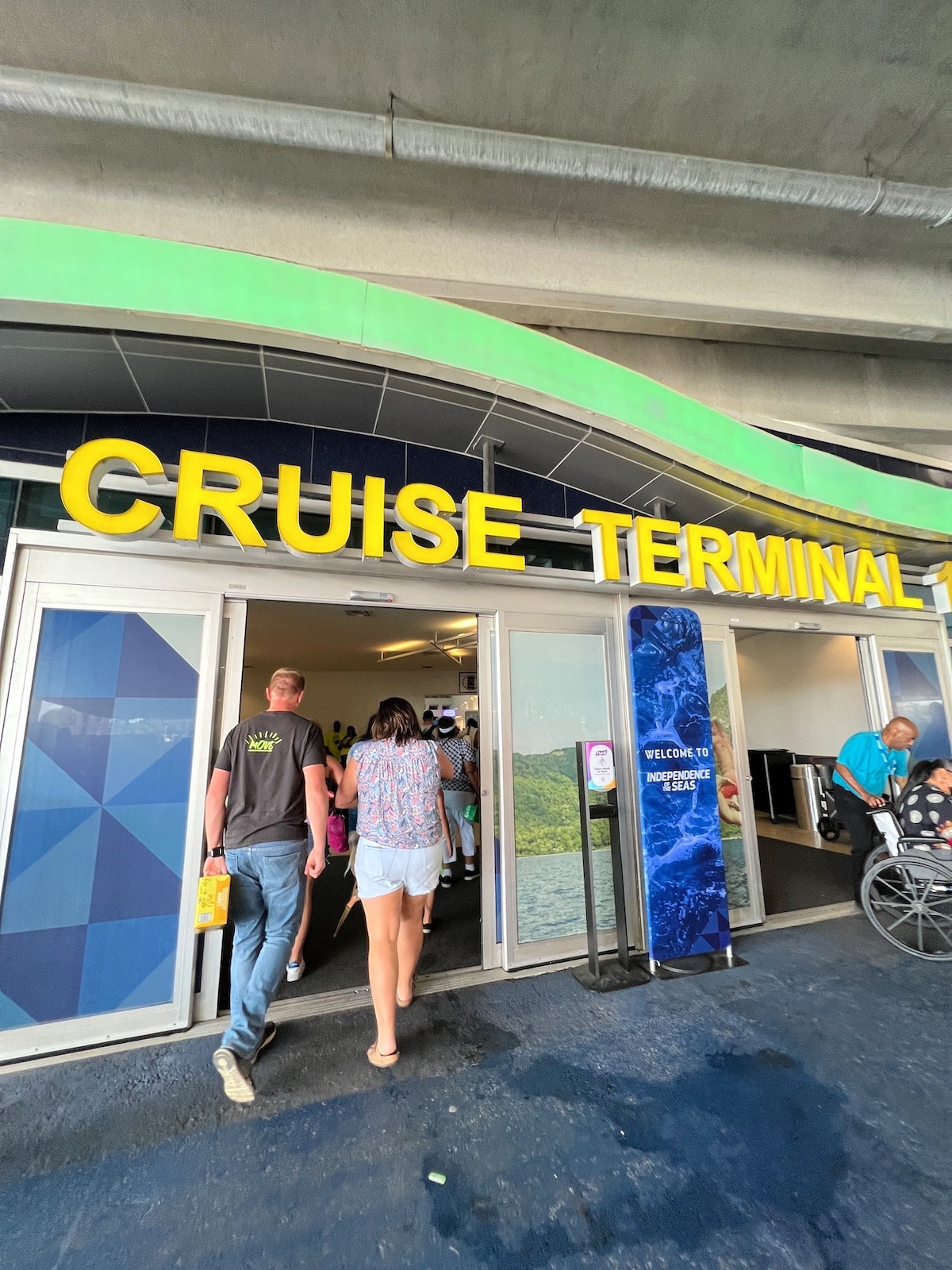 People walking into a building with a sign above that reads "CRUISE TERMINAL." A wheelchair-user is visible on the right side near the entrance.