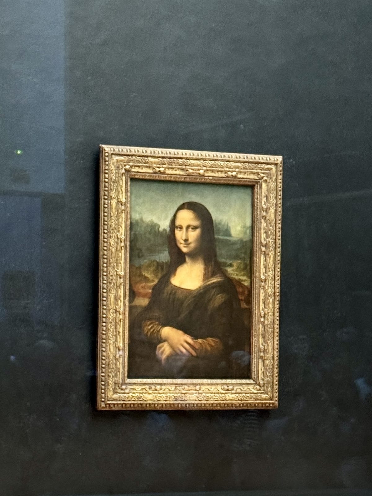 A framed painting of the Mona Lisa displayed on a dark wall evokes the charm of one day in Paris. The subject is a woman with long hair, a faint smile, and folded hands. The background features a serene landscape.