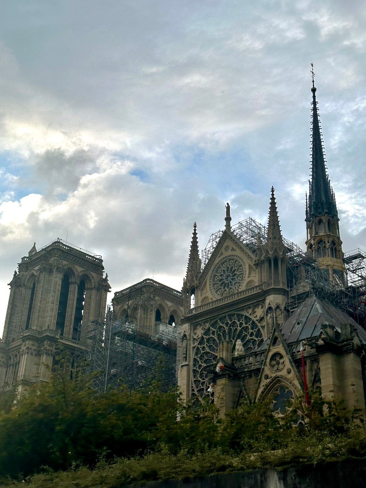 Gothic cathedral with scaffolding, featuring a tall spire, intricate facade, and two towers, under a partly cloudy sky—one day in Paris you won't forget.