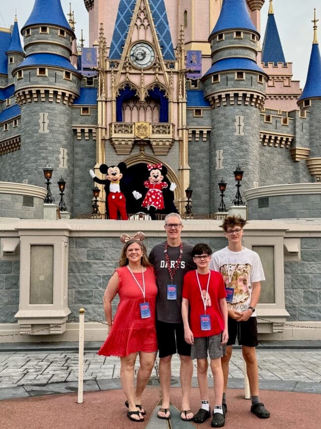A family of four stands in front of a castle with two costumed characters on stage, all wearing visitor passes around their necks, as if posing for a scene straight out of Andrea Updyke's blog.