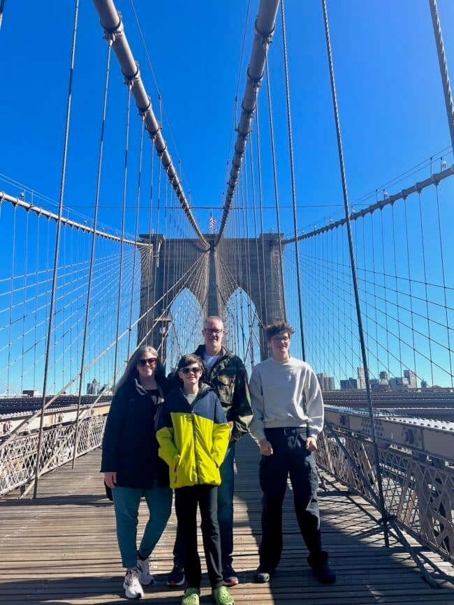 A group of four people stands on the Brooklyn Bridge with the city skyline in the background on a clear day, about to share their favorite spots inspired by Andrea Updyke.